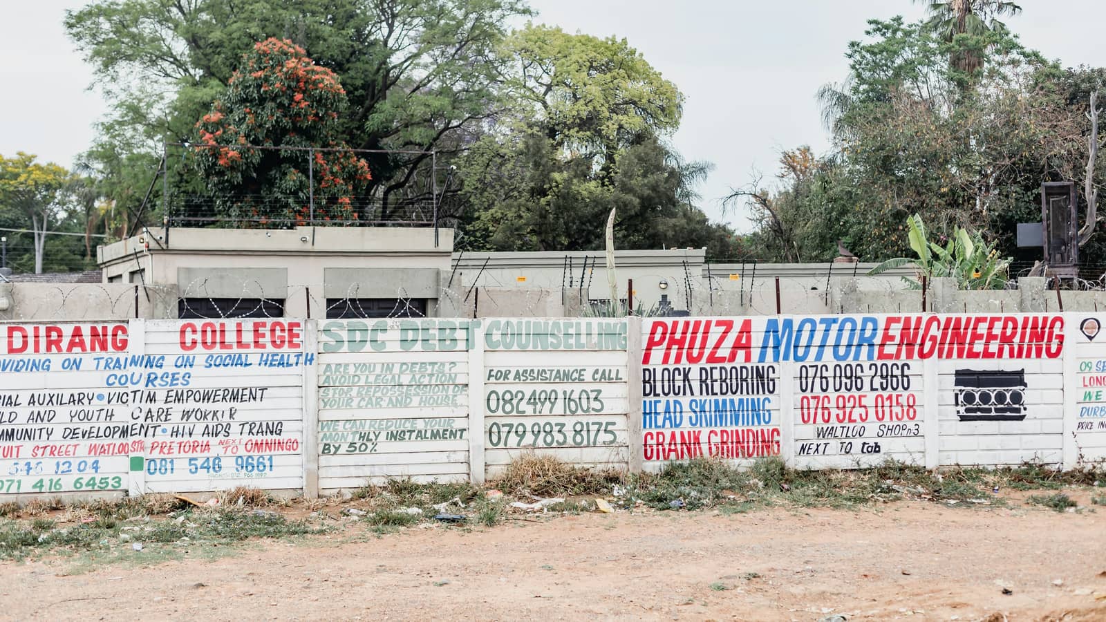 A roadside wall covered in hand-painted signs advertising local businesses