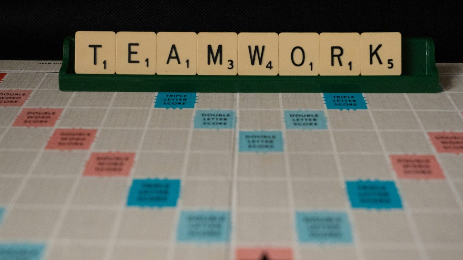Scrabble tiles spelling TEAMWORK on a rack above a Scrabble board