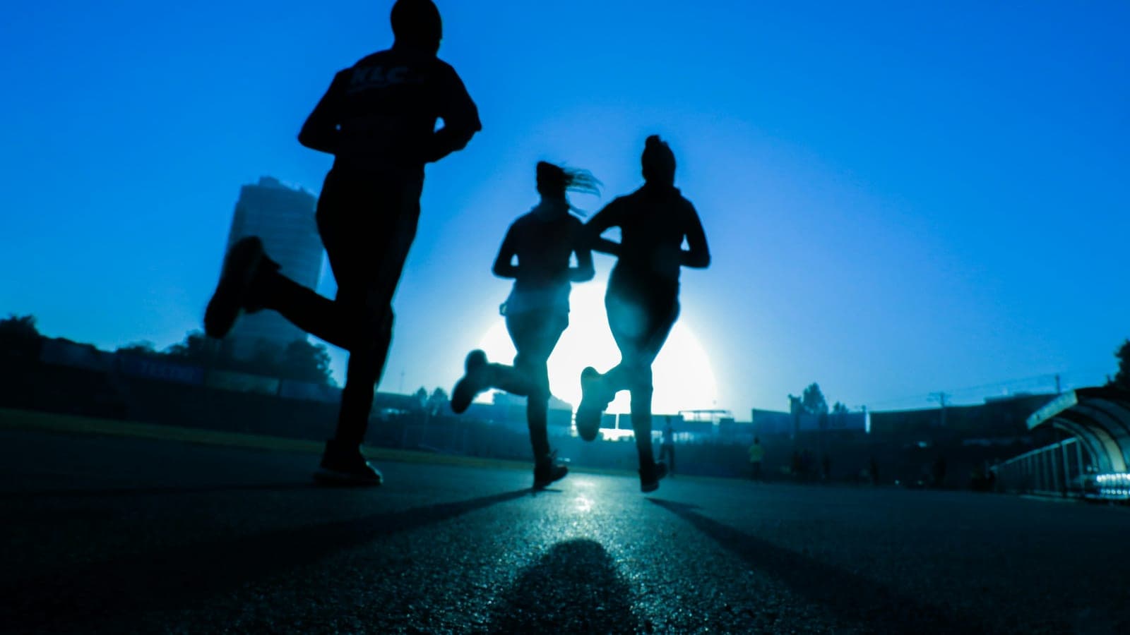 Silhouette of three women running on grey concrete road
