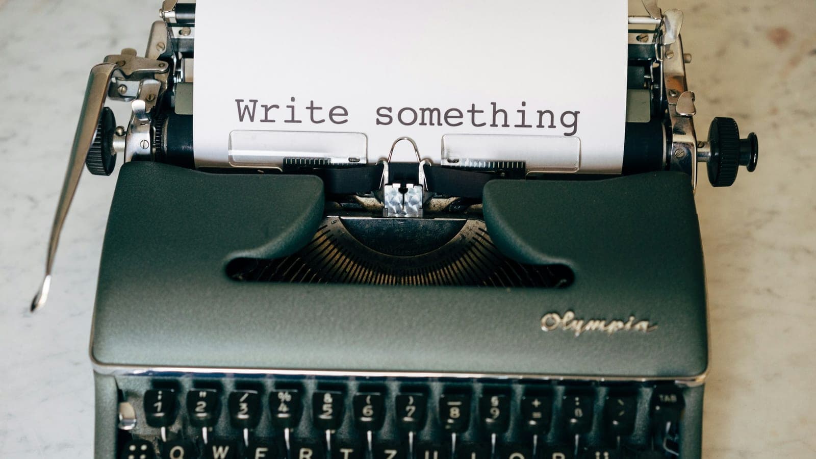 An Olympia typewriter with paper reading "Write something" on a marble surface