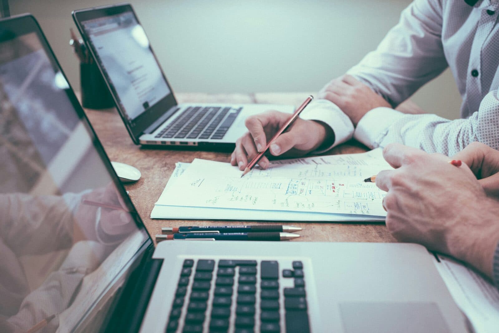 Two consultants reviewing handwritten notes at a table with open laptops — representing the organized engagement knowledge layer that makes AI tools effective in advisory practices