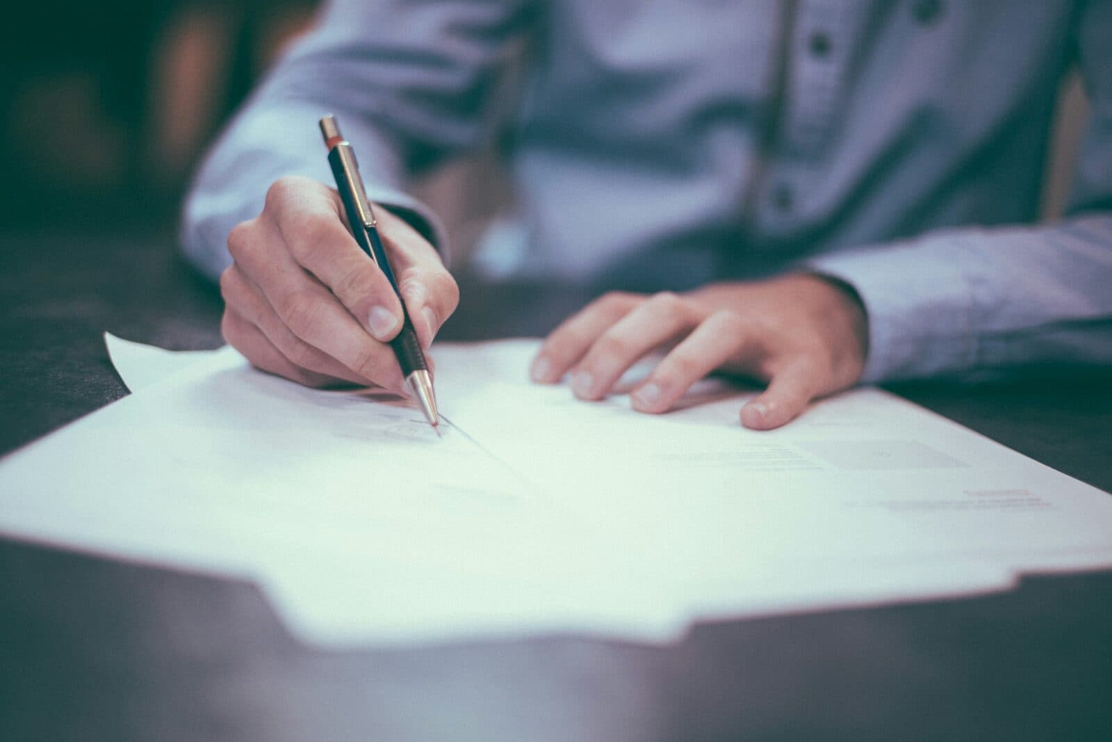 A professional writing on a document at a desk, pen in hand, with a blurred office background