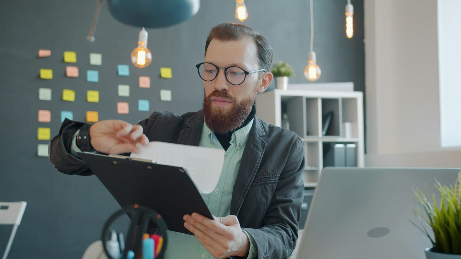 A professional in glasses reviewing structured documents at a clean, organized desk with a laptop open beside them