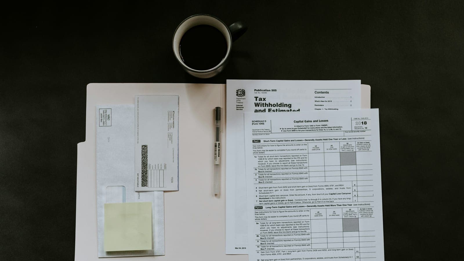 Tax forms, a pen, and a coffee mug on a dark desk