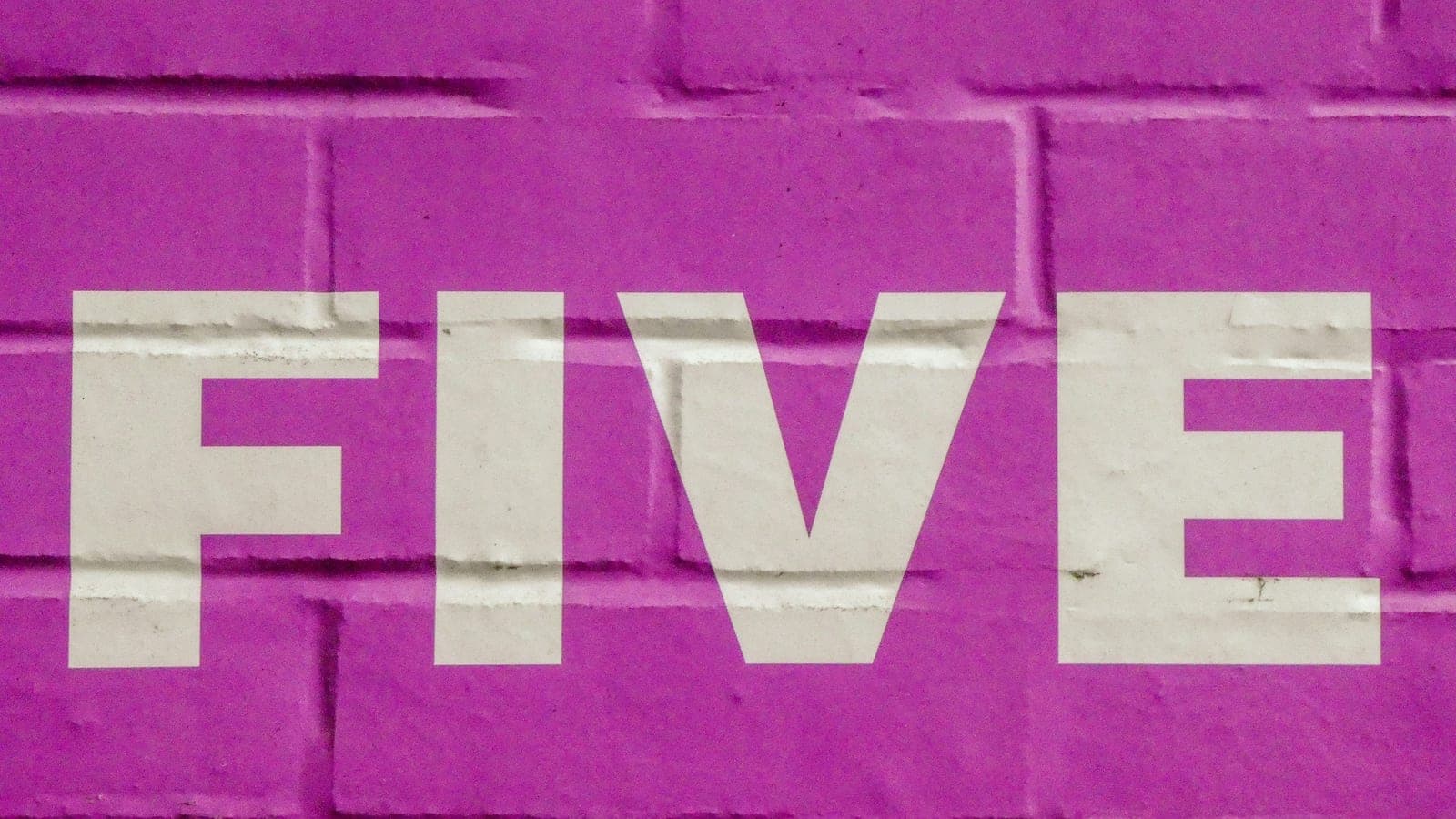 The word five in white letters on a pink brick wall.