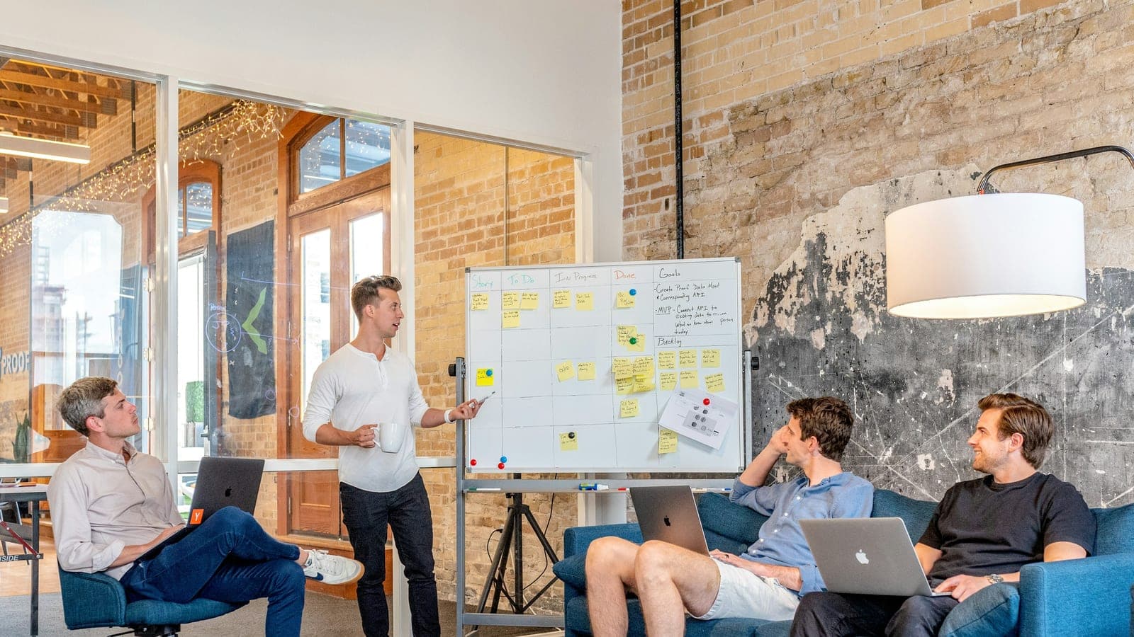 Three men sitting while using laptops and watching man beside whiteboard